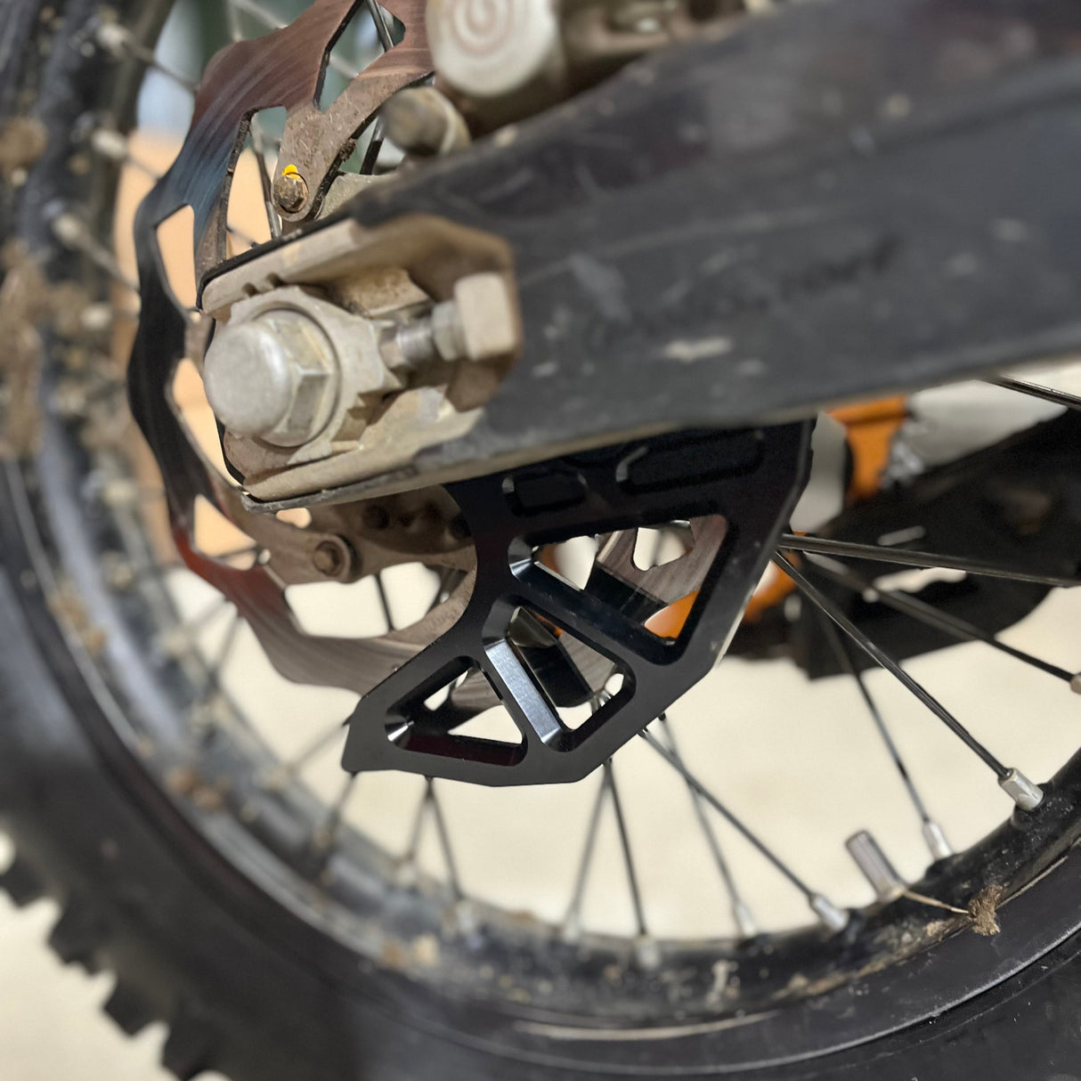 Side‑angle shot of the black anodised aluminium rear brake disc guard mounted on a KTM bike, highlighting its sleek profile and how it protects the disc and caliper.