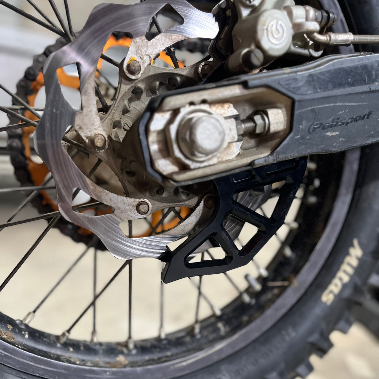Close‑up of the rear brake disc guard showing the caliper support built into the anodised aluminium structure, demonstrating the guard’s functional design.