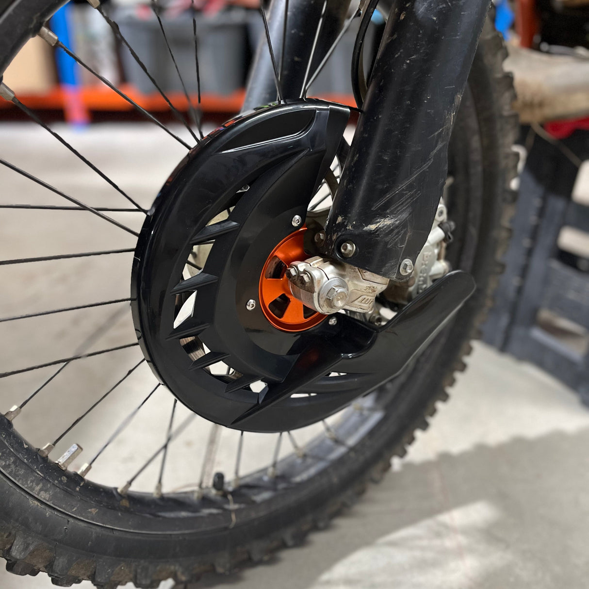 Front view of the front brake disc guard for KTM 125–530 (2015–2024), featuring an orange anodized 6061-T6 aluminium hub and black high-impact polypropylene shield.