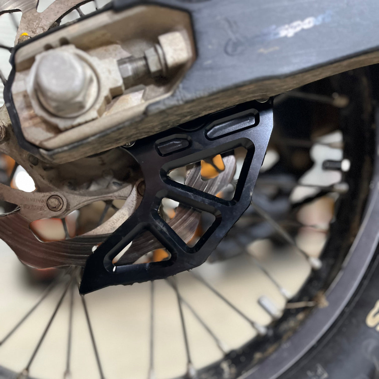 Laydown display of the aluminium rear brake disc guard components: black anodised guard, hardware for installation, and instructions—ready for KTM 2005–2023 models.