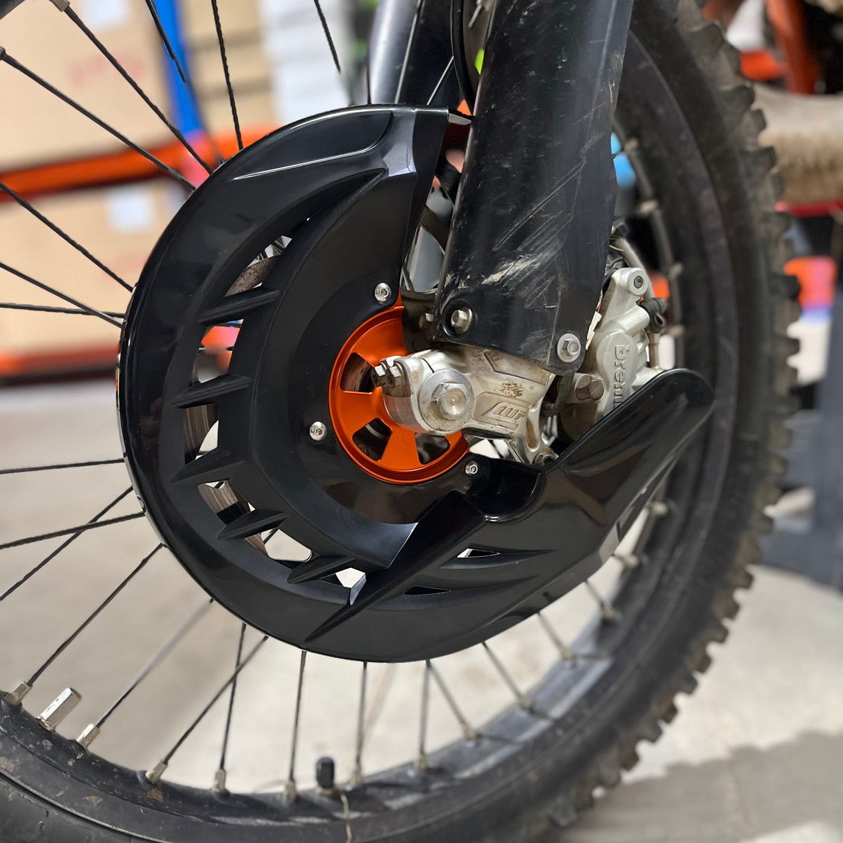 Angled side view of the KTM brake disc protector showing the profile of the orange aluminium hub and black protective shield.